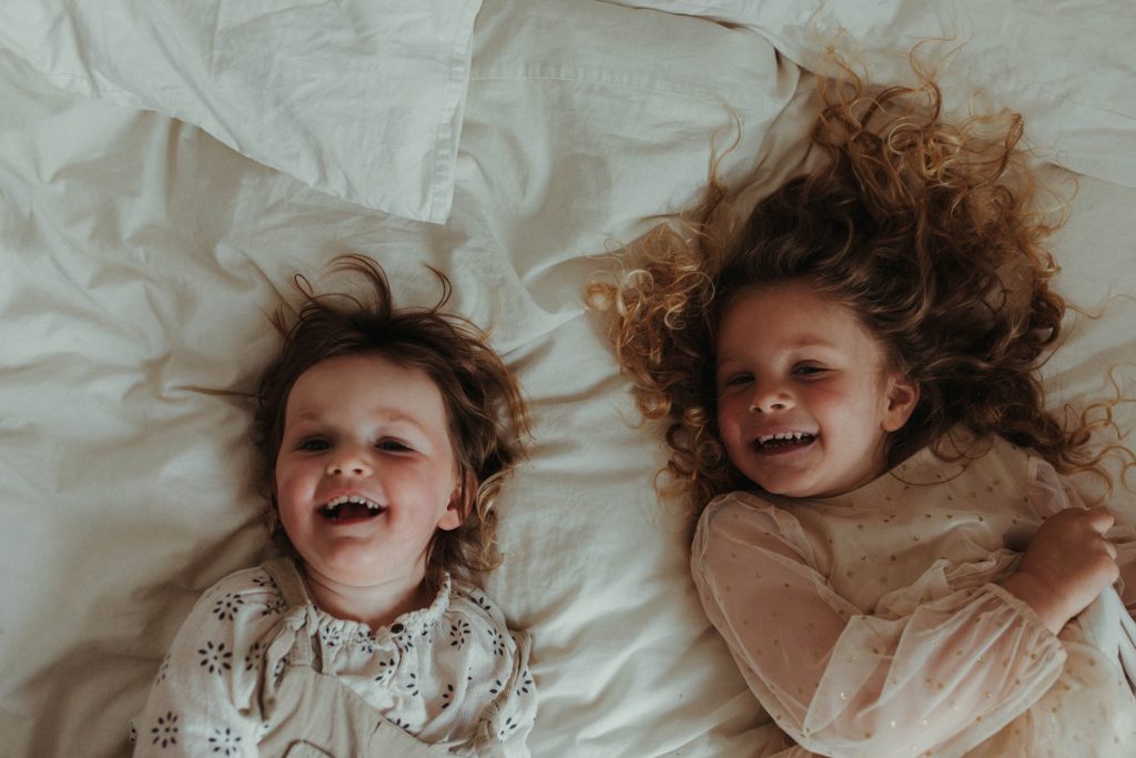 portrait photographer cornwall 2 toddlers laughing on bed linens being photographed at a family session