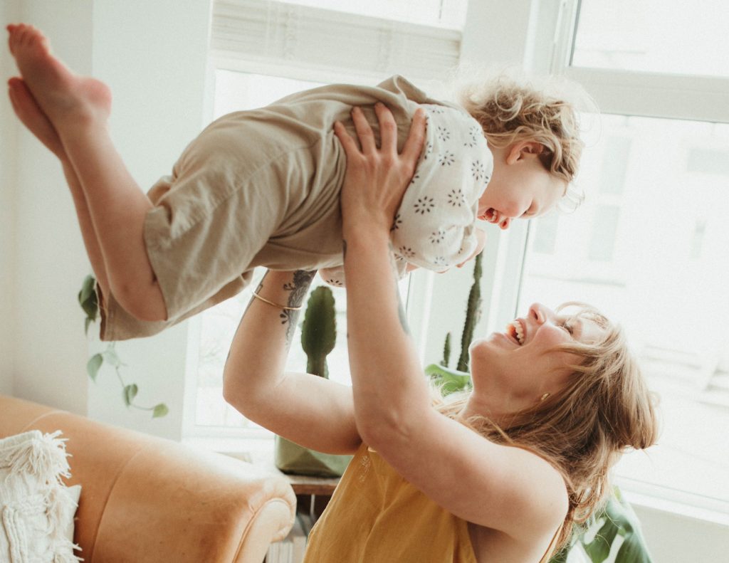portrait photographer cornwall toddler laughing being lifted in air by mum while being photographed at a family session at home