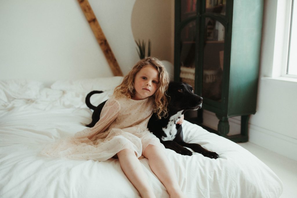 portrait photographer cornwall toddler with dog on bed photographed at a family session at home