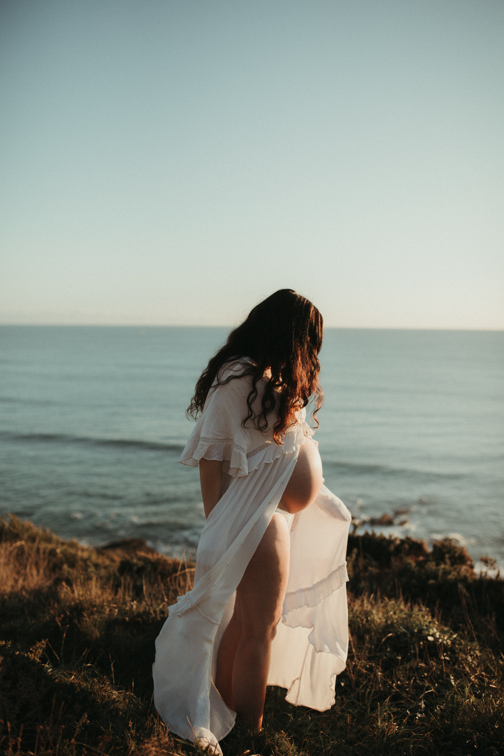 Pregnant woman sways in the sand dunes in white dress
