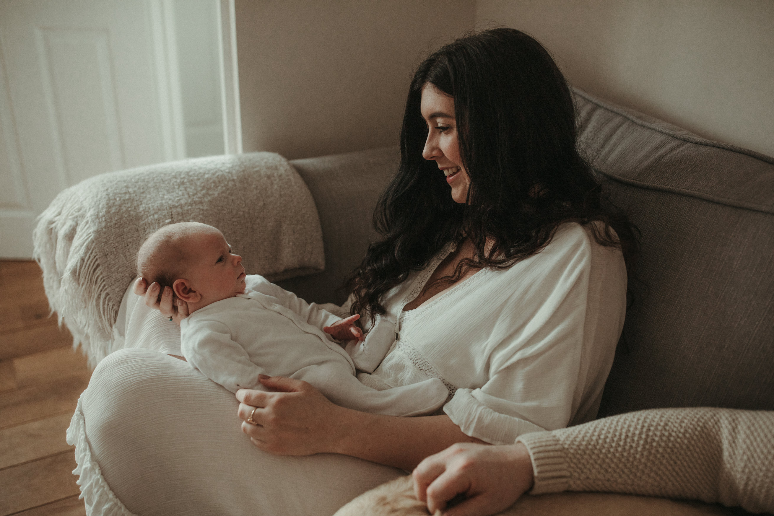 New mother gazes down at baby on their sofa at home Maternity and Newborn Photographer Devon 