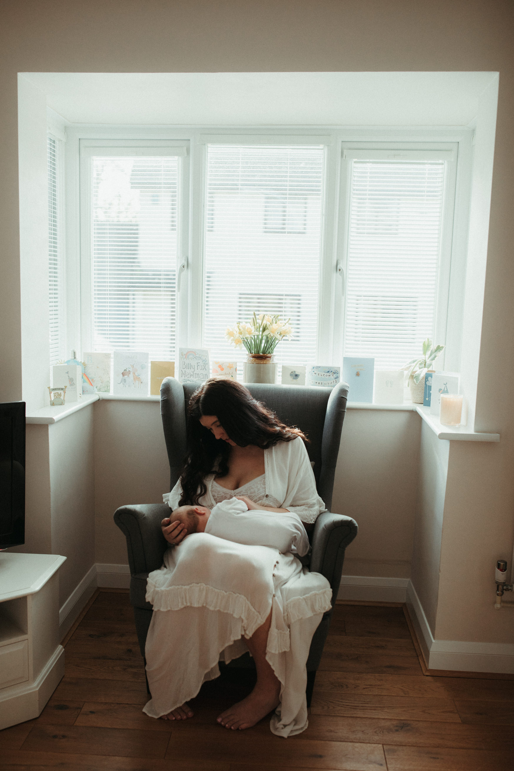 mother sits in armchair by the window gazing at newborn 