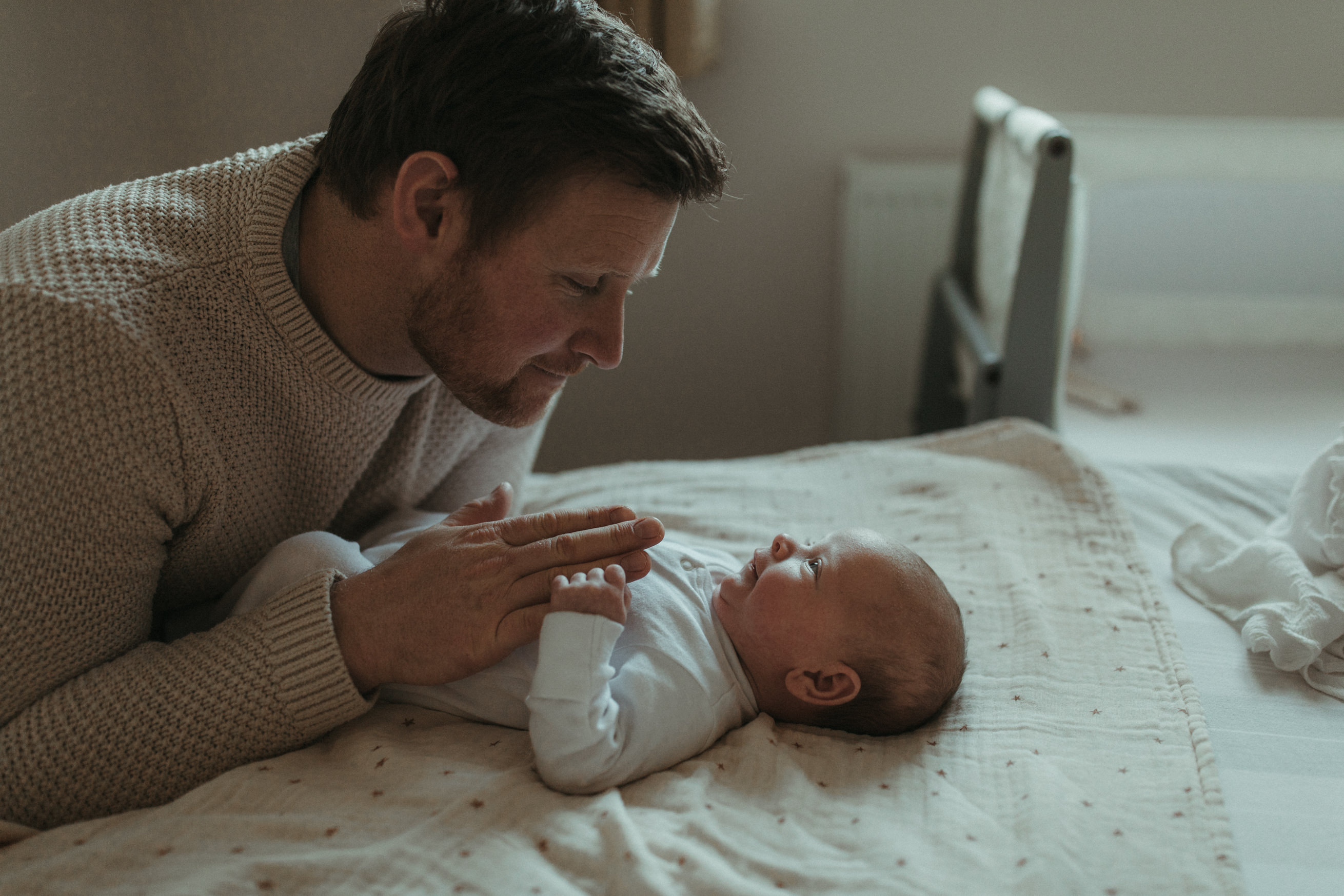 New dad smiles down at baby on bed Maternity and Newborn Photographer Devon 