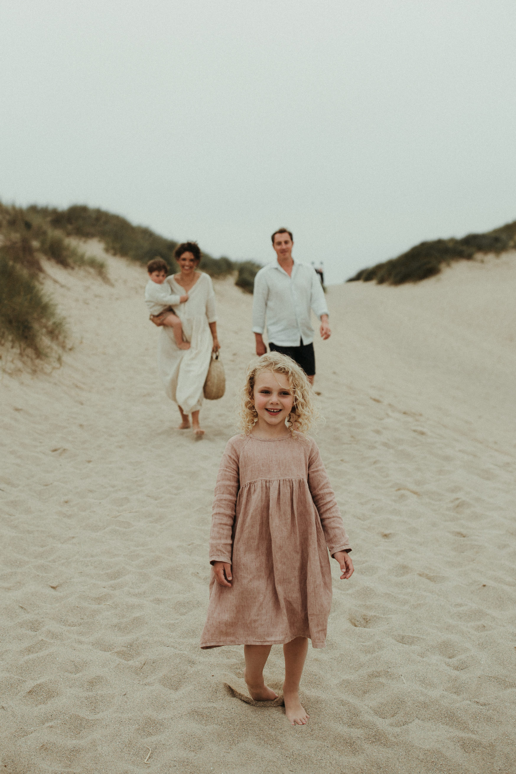 family walk towards camera with little girl in foreground at the beach during lifestyle family photography session