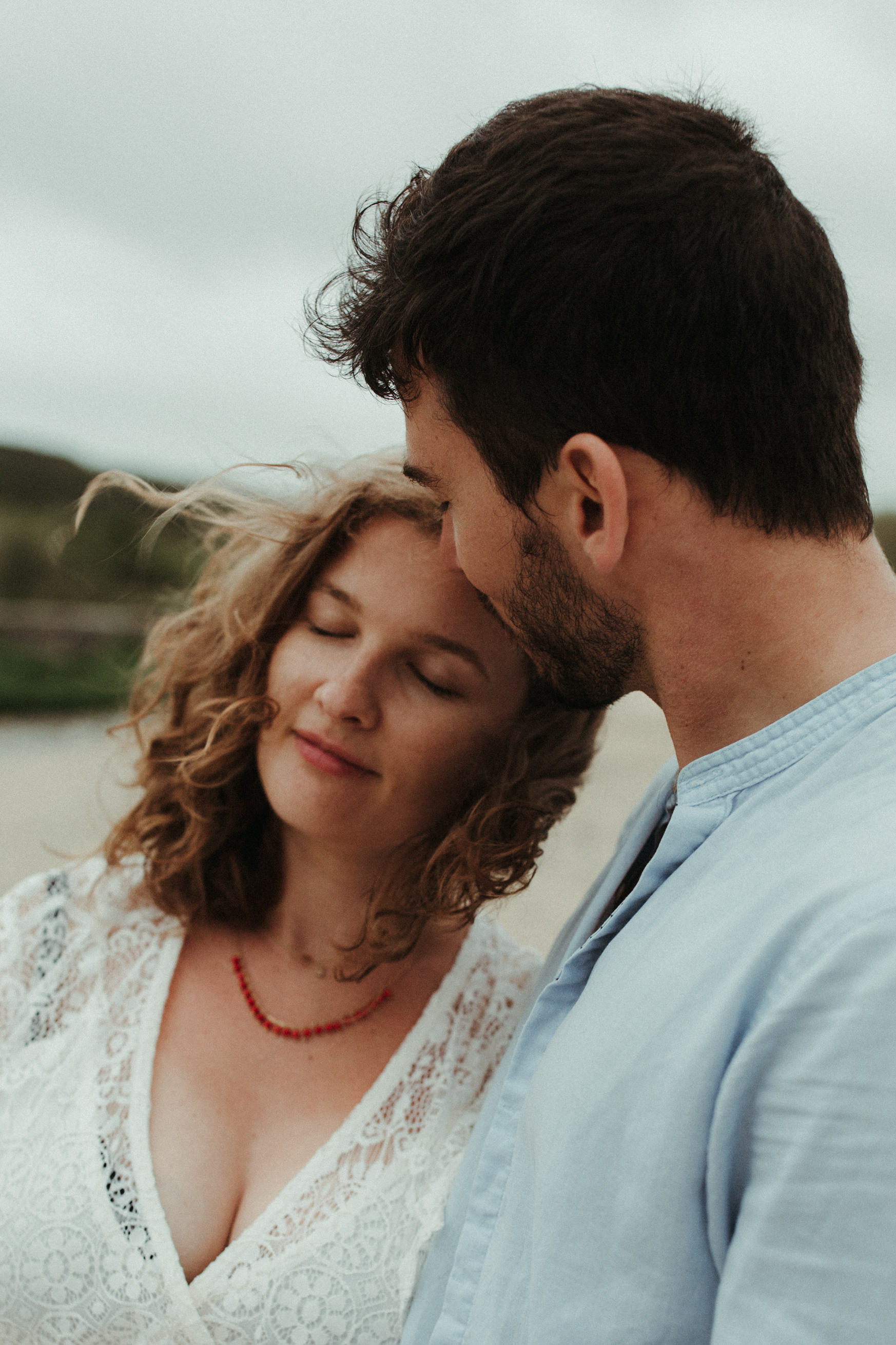woman leans into man with her eyes closed as he kisses her forehead