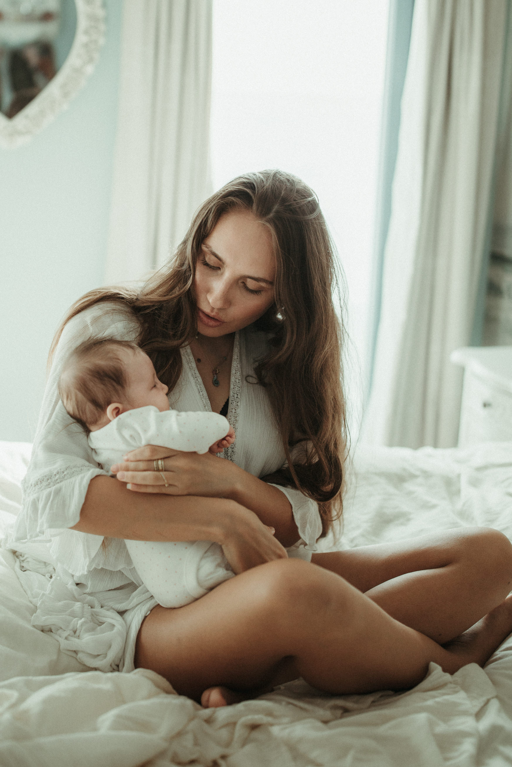 Mother holds baby in arms on bed and shushes it Natural baby photography devon