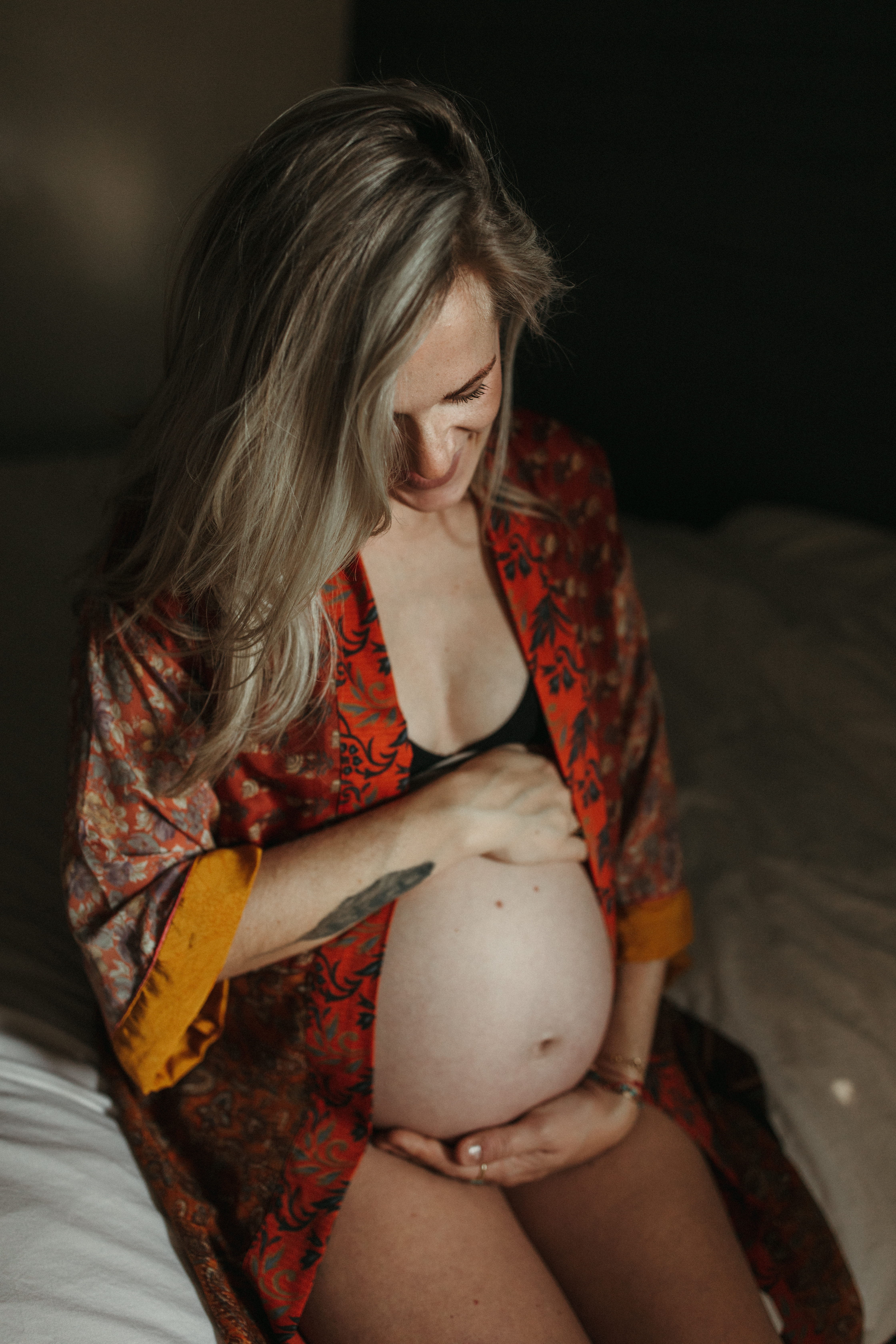 women sits holding pregnant stomach in beautiful red boho dressing gown