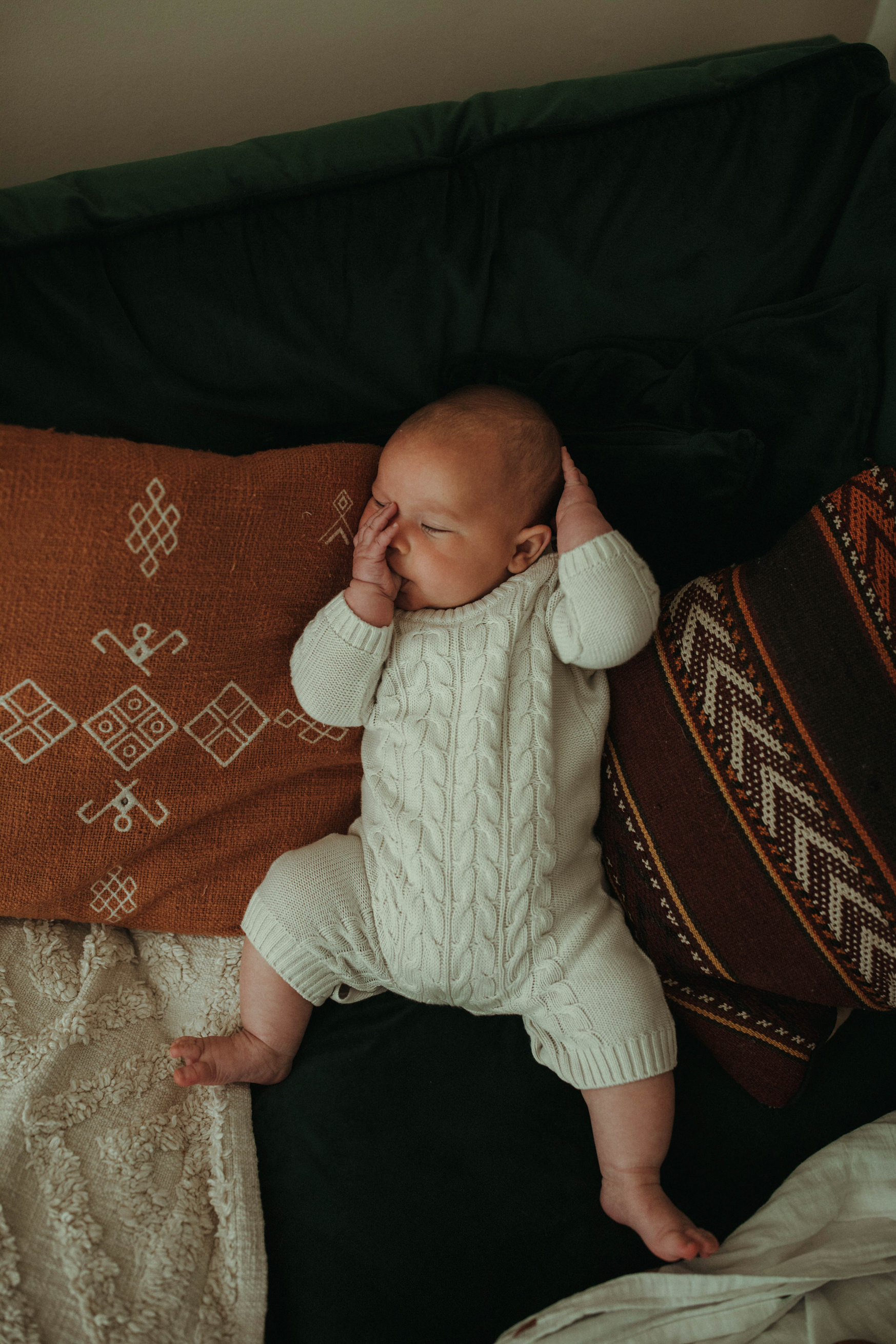 baby sucking thumb lying on sofa inbetween cushions