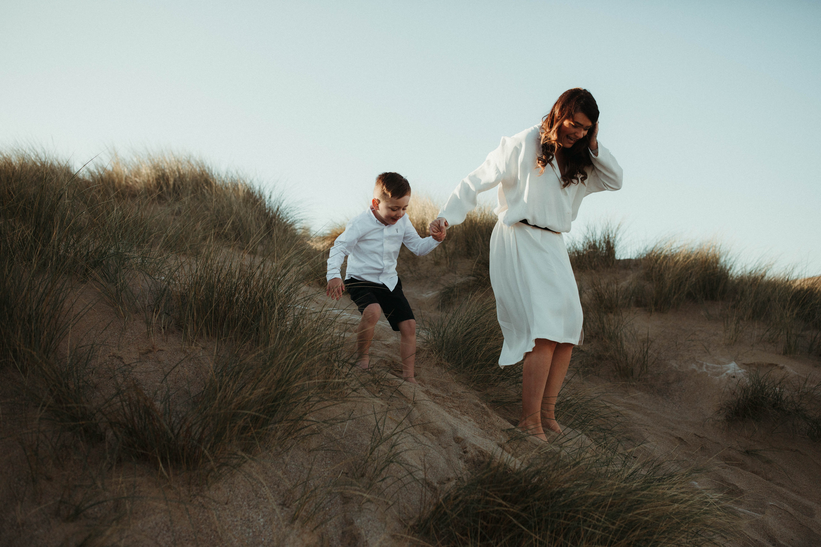 Mother holds sons hand as they walk down sand dunes at the beach