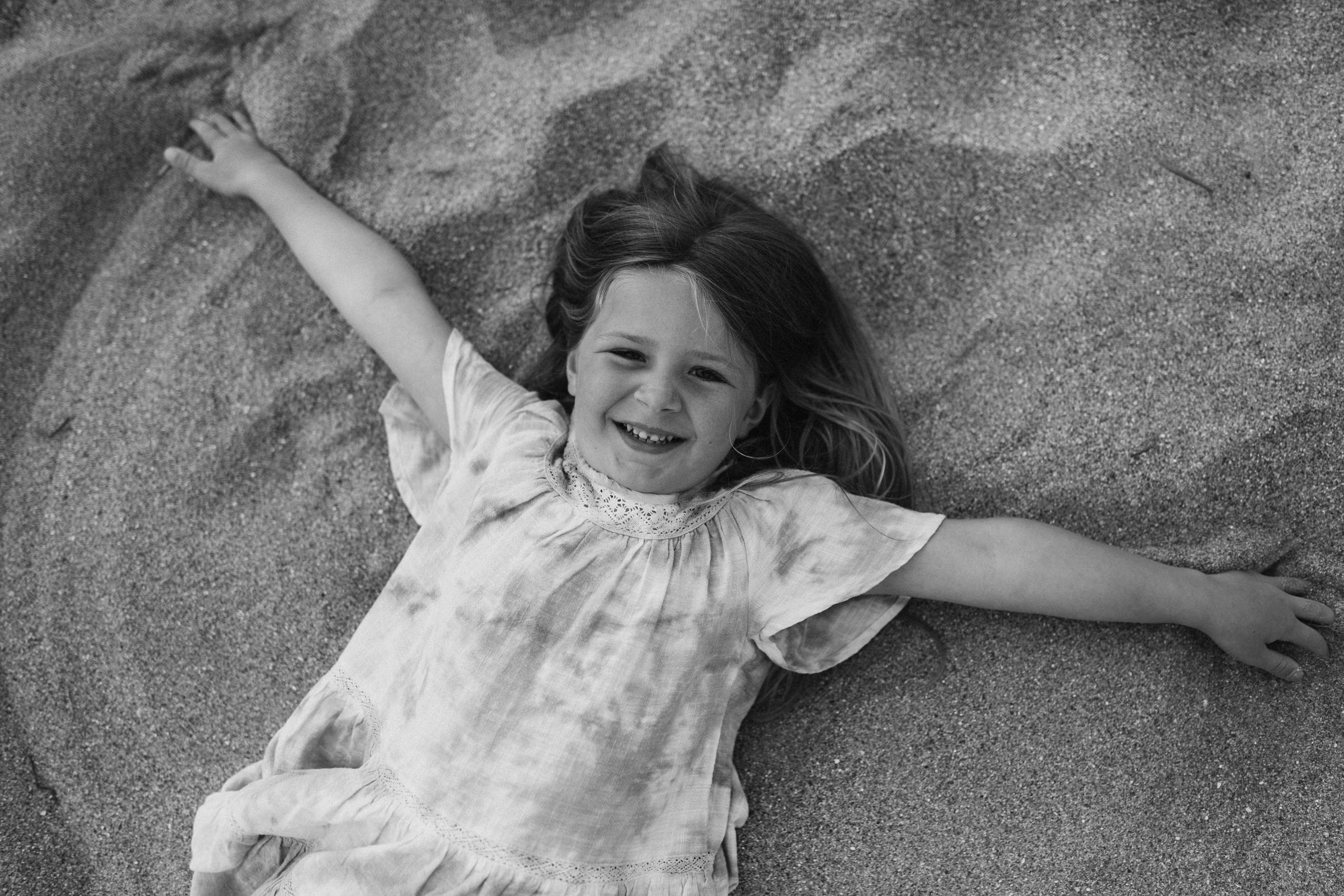 Little girl looks up at camera and runs hands through sand