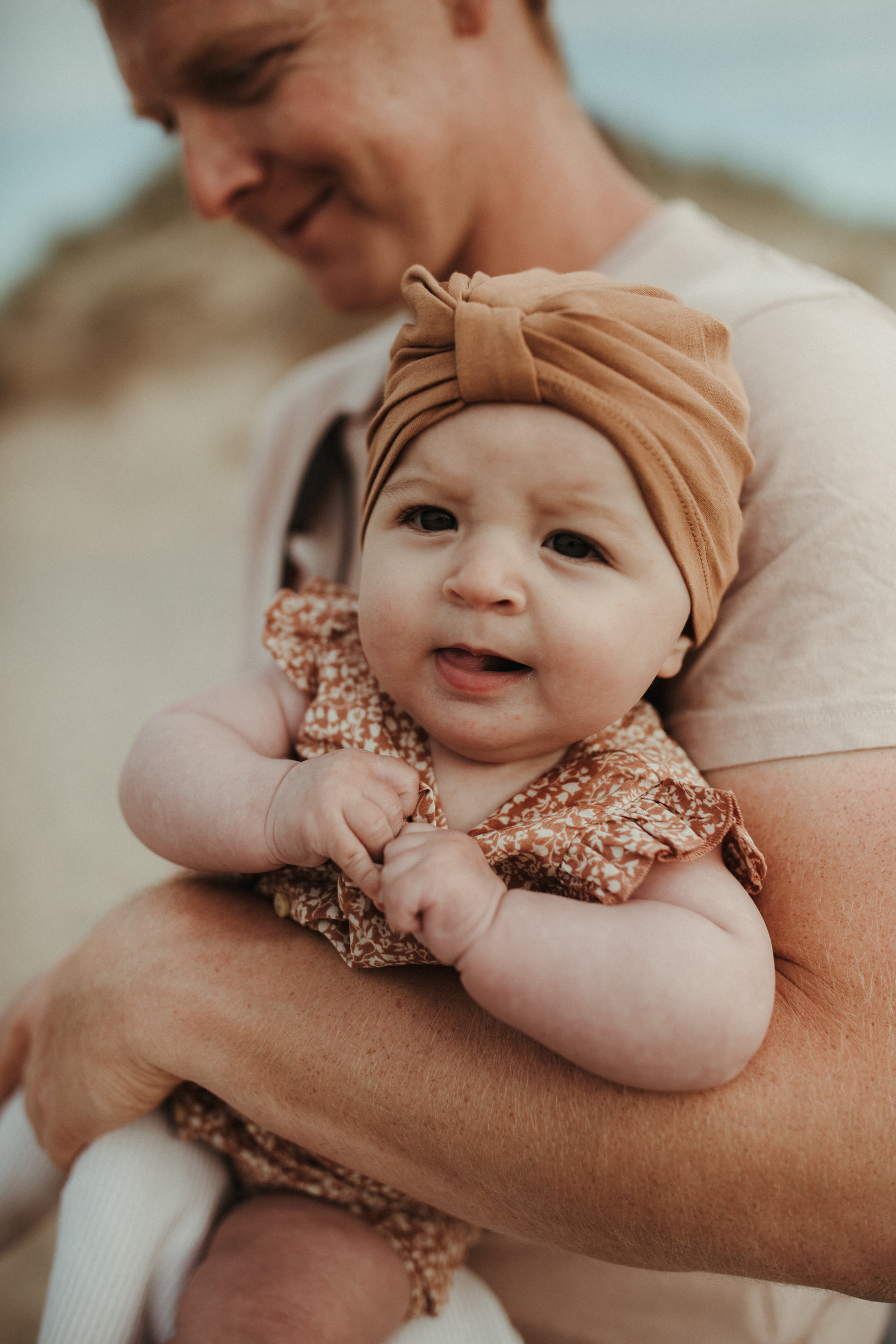 Baby in head wrap looks at camera for boho family photos