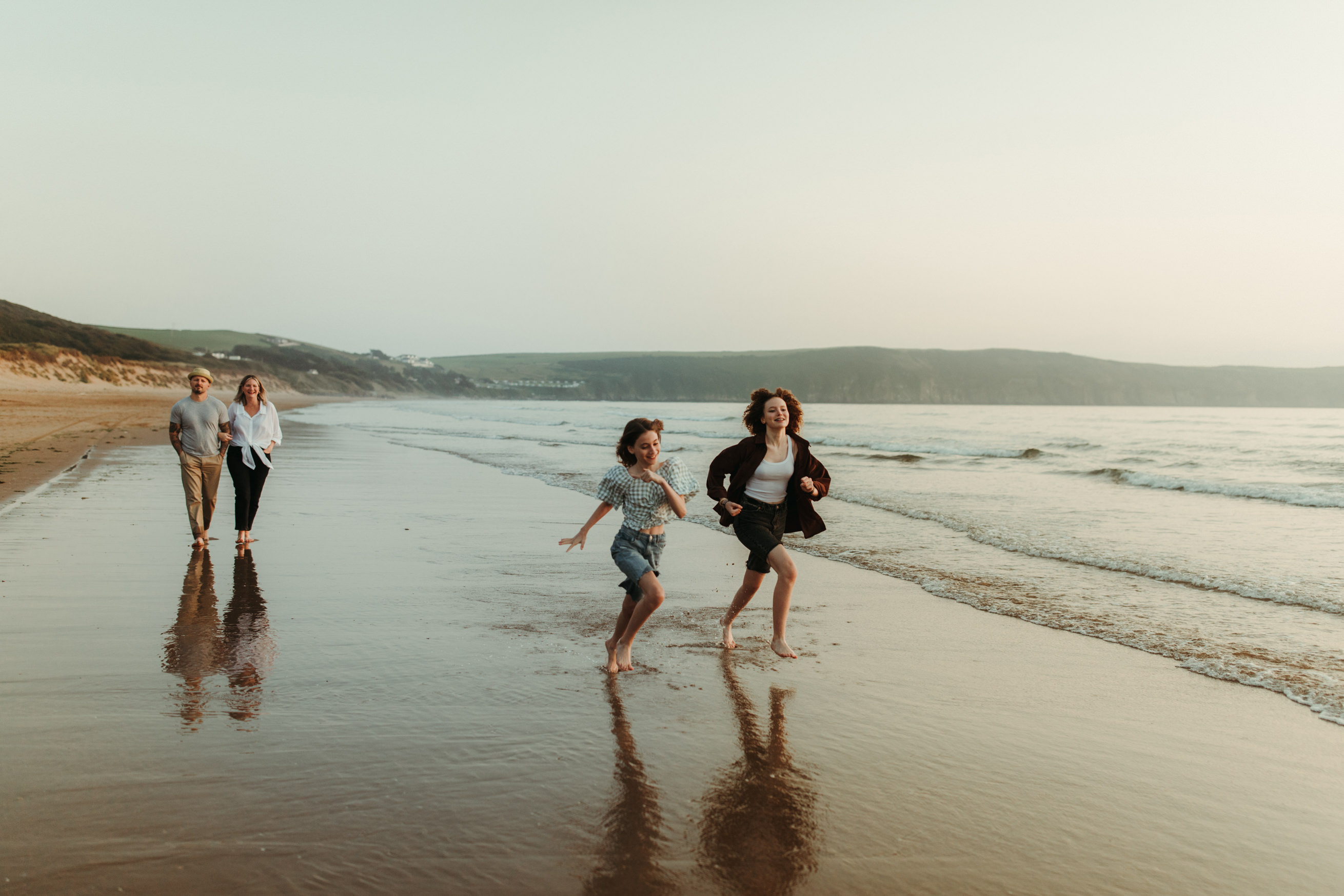 Sisters run on the beach as parents walk behind looking on