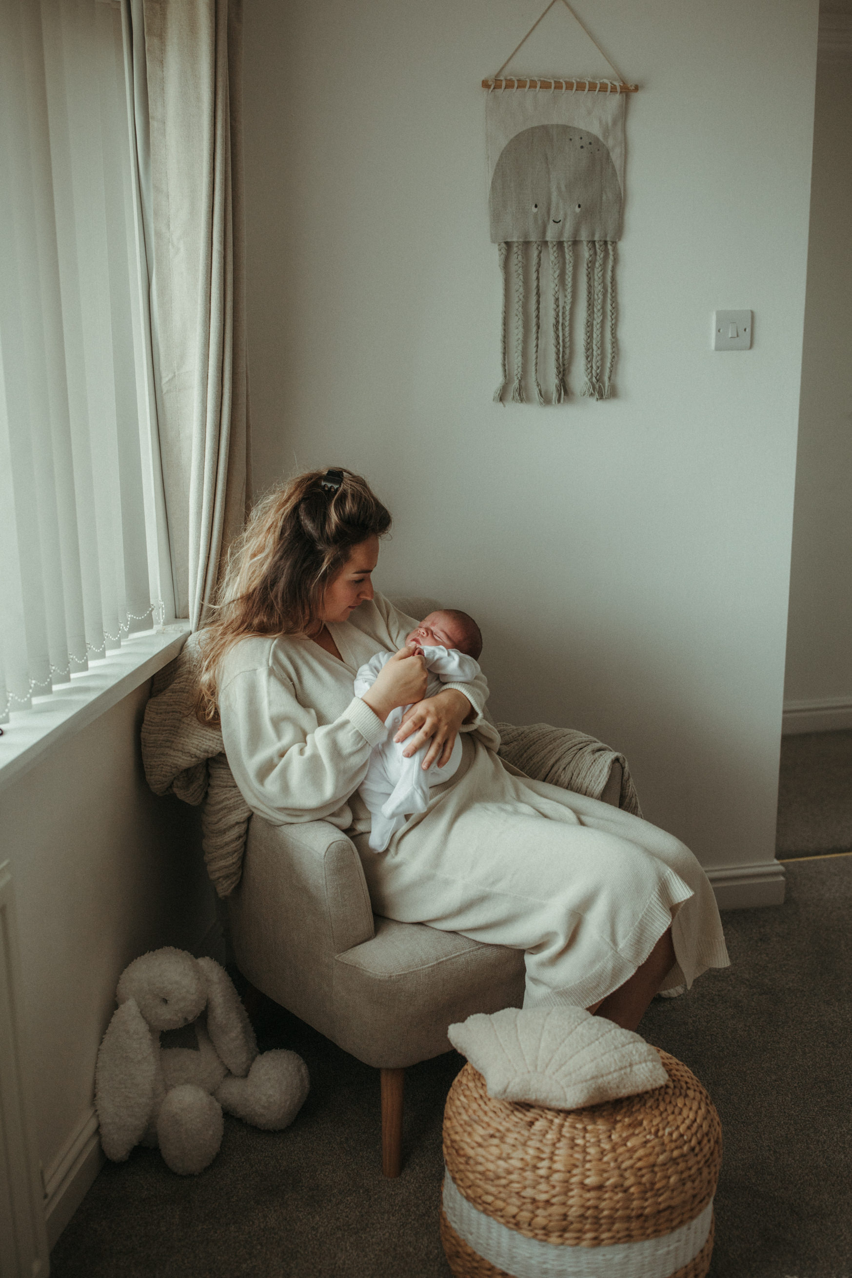 Mother holds baby in arms on armchair in nursery Baby Photography Cornwall