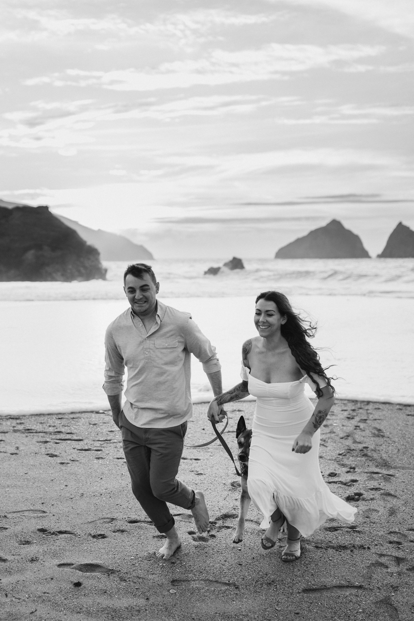 black and white shot of man and woman running from the sea during cornwall couples photoshoot