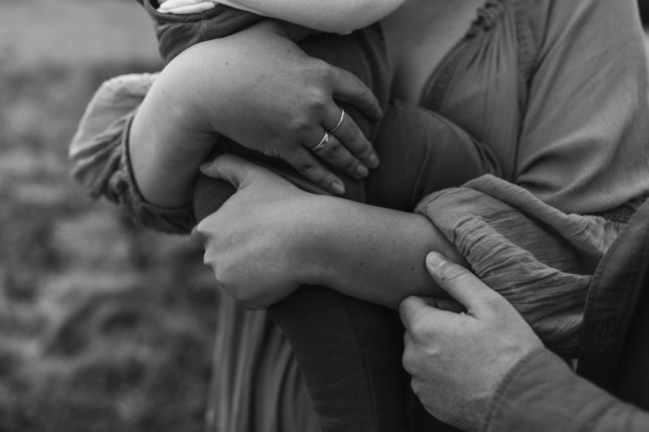 A black and white close up image of a mothers hands holding her toddler son.