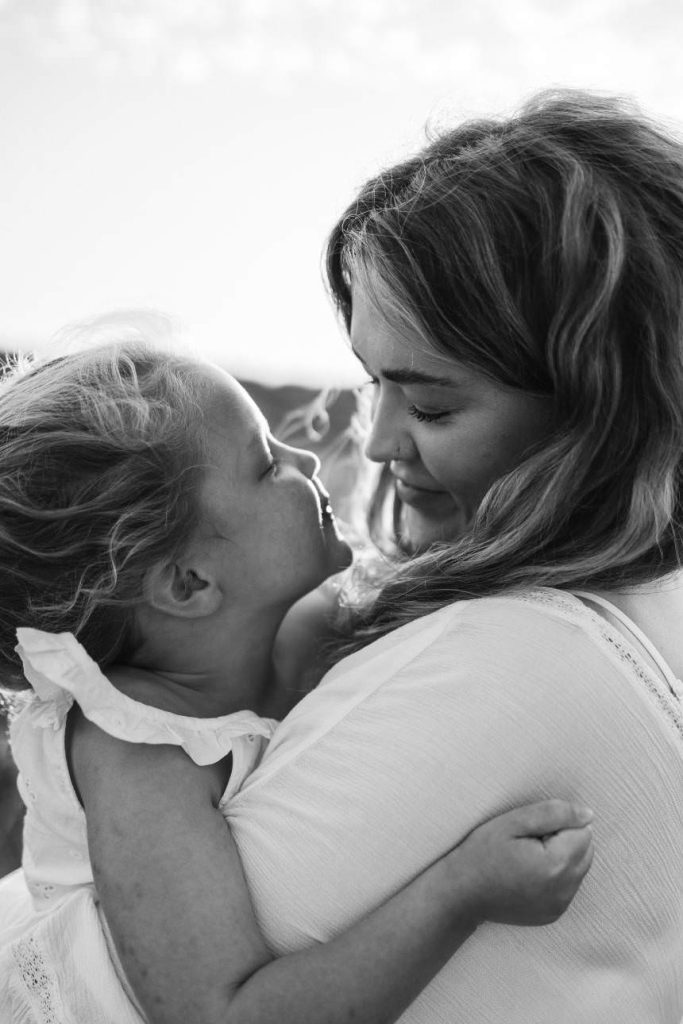 A black and white image of a little girl cuddling her mother, their faces are close together and the mother is looking adoringly at her daughter.